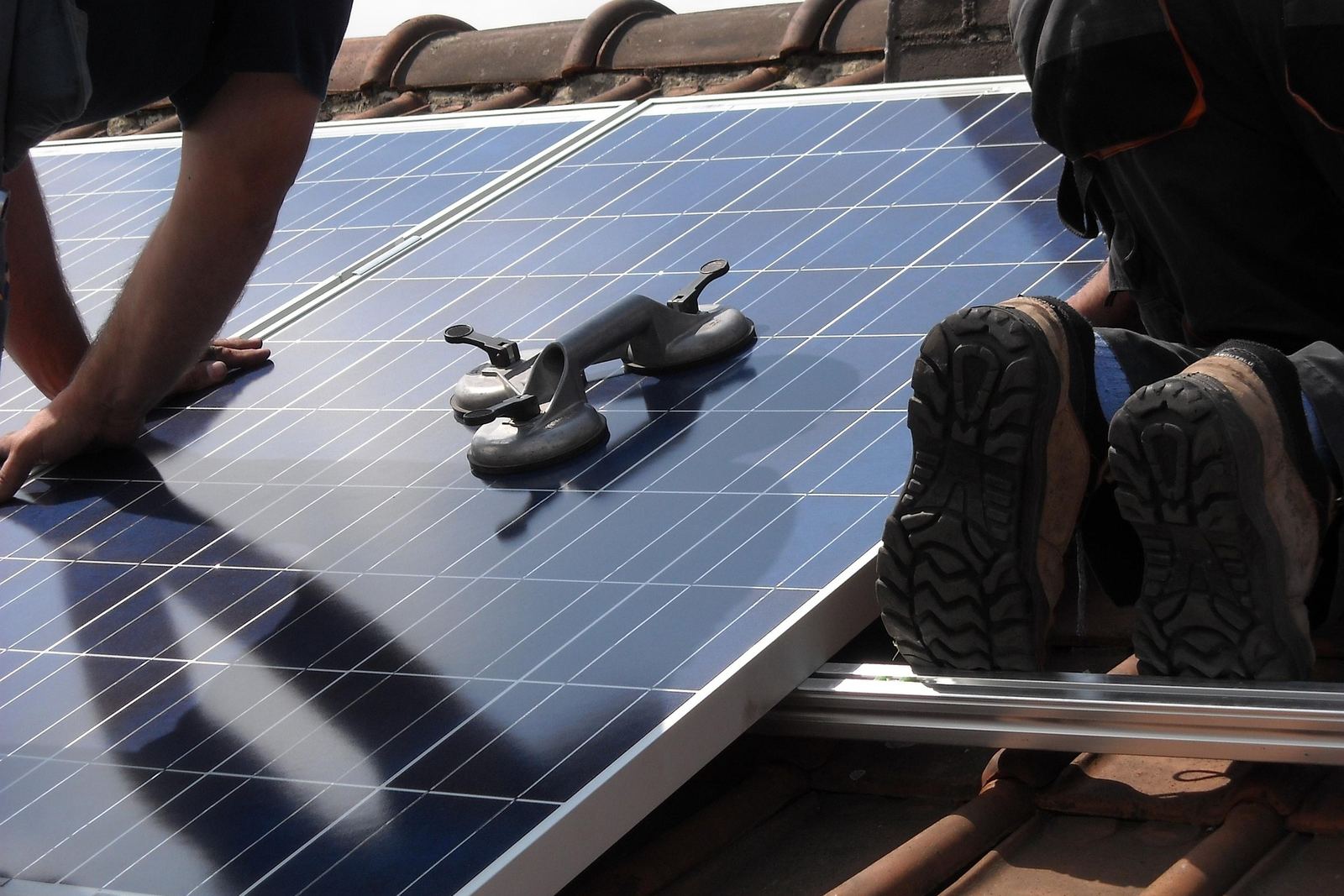 Two installers seating a panel onto its rail on a tiled roof